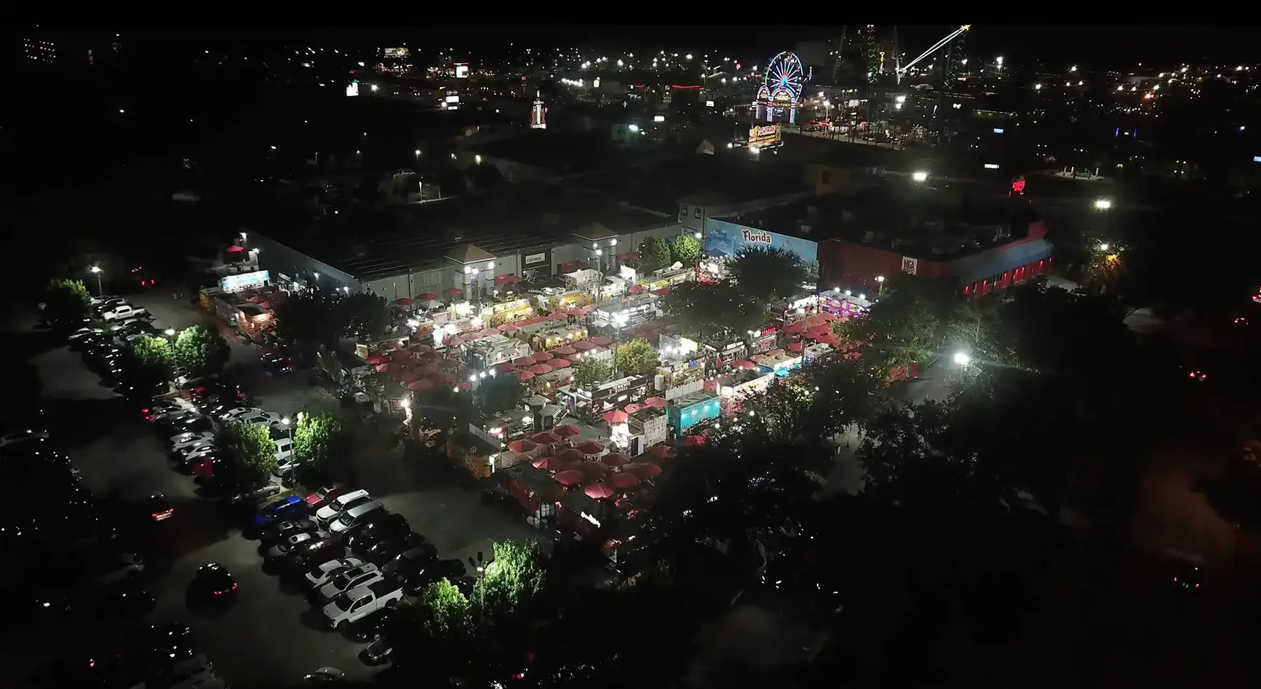 The plaza from the air at night, the food truck park glowing with string lights and the lot full of cars.