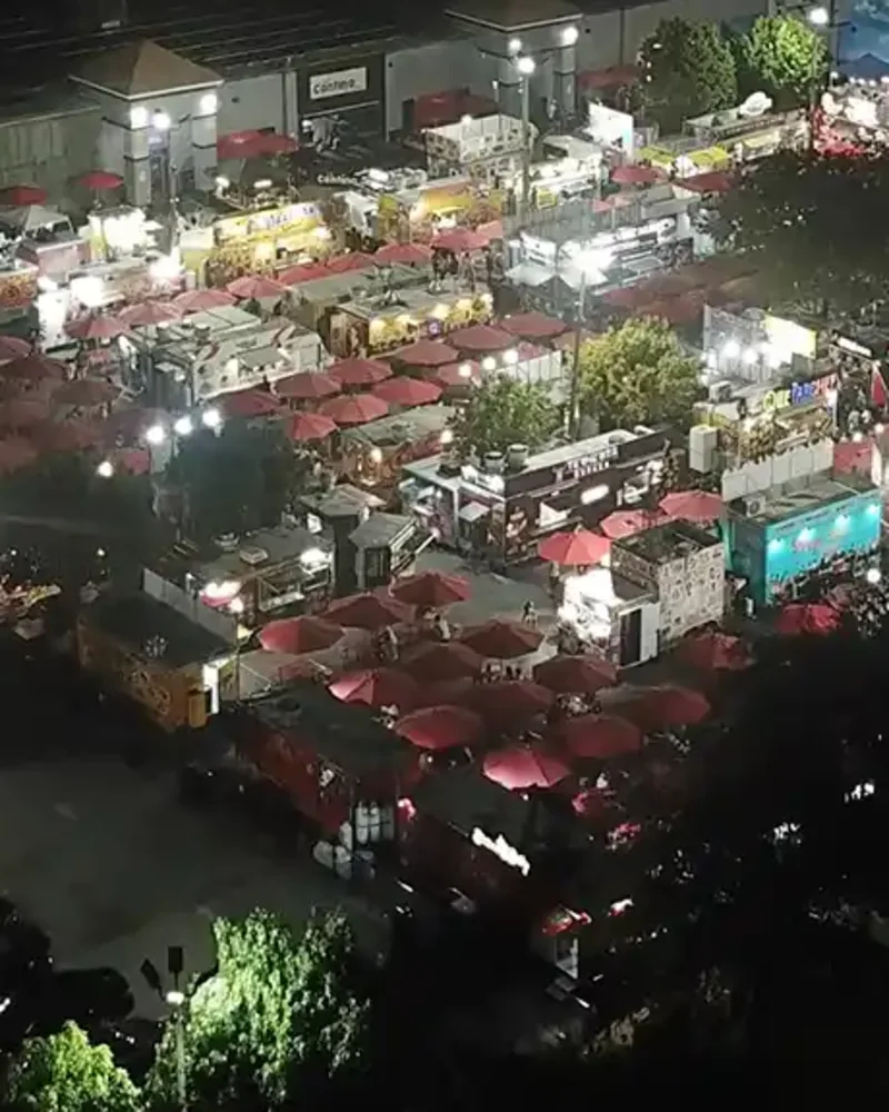A food truck parked under red umbrellas in the park behind the plaza.